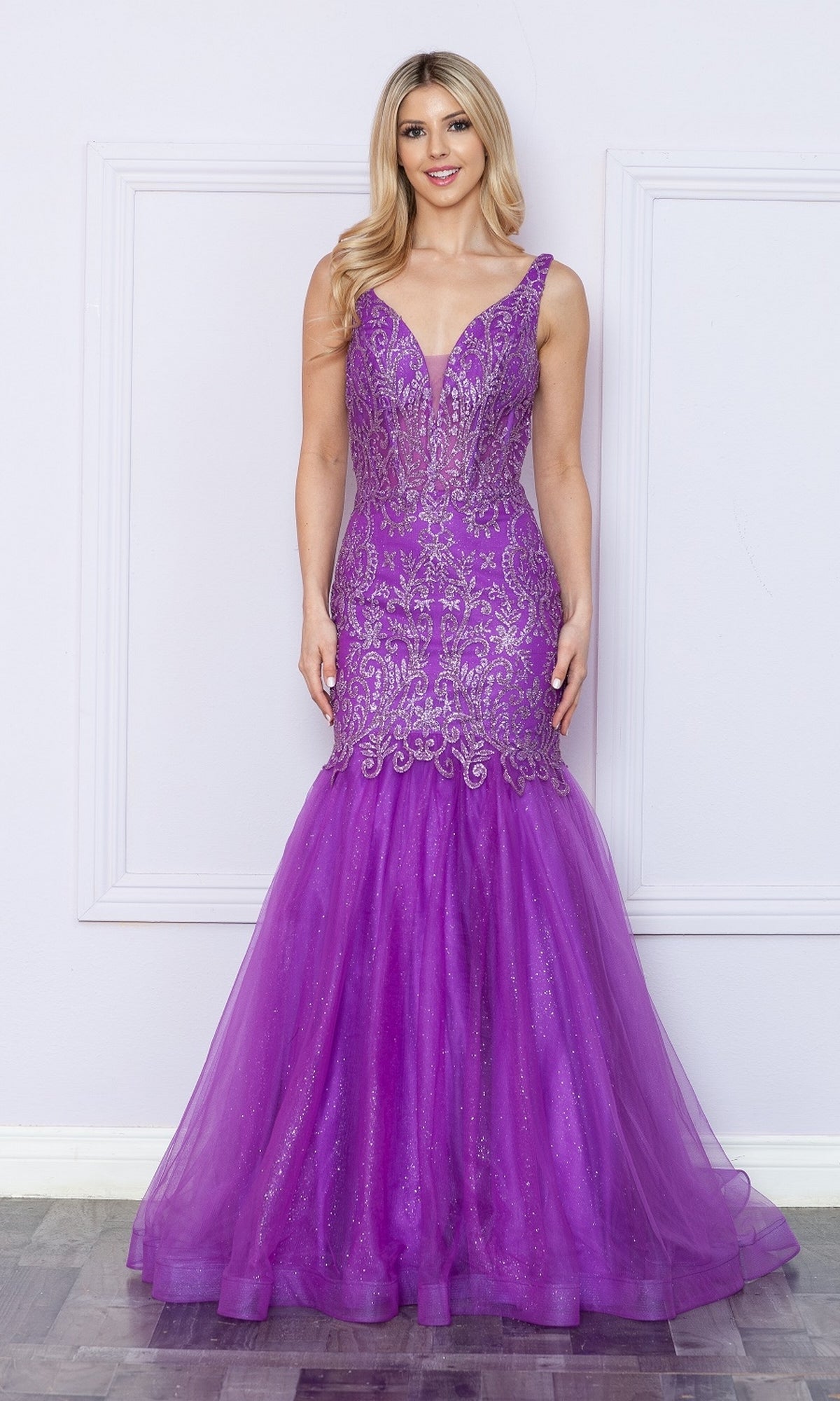 Woman in a fitted, sleeveless Low V-Neck Long Glitter Mermaid Prom Dress 9388 with intricate silver embellishments and subtle glitter print stands against a light-colored wall.